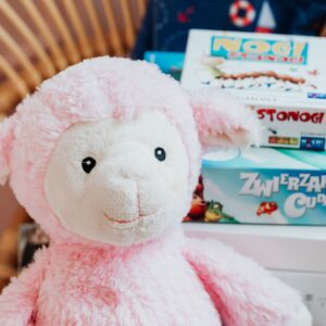 Home Close-up of a pink plush lamb alongside colorful board games, perfect for children's playrooms.